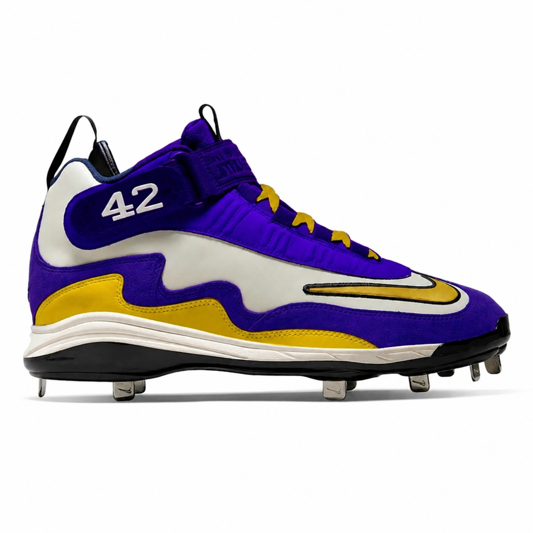 A Nike baseball cleat in purple, white, and gold, featuring the number 42 on the side, a gold Nike Swoosh, and metal cleats on a white background.