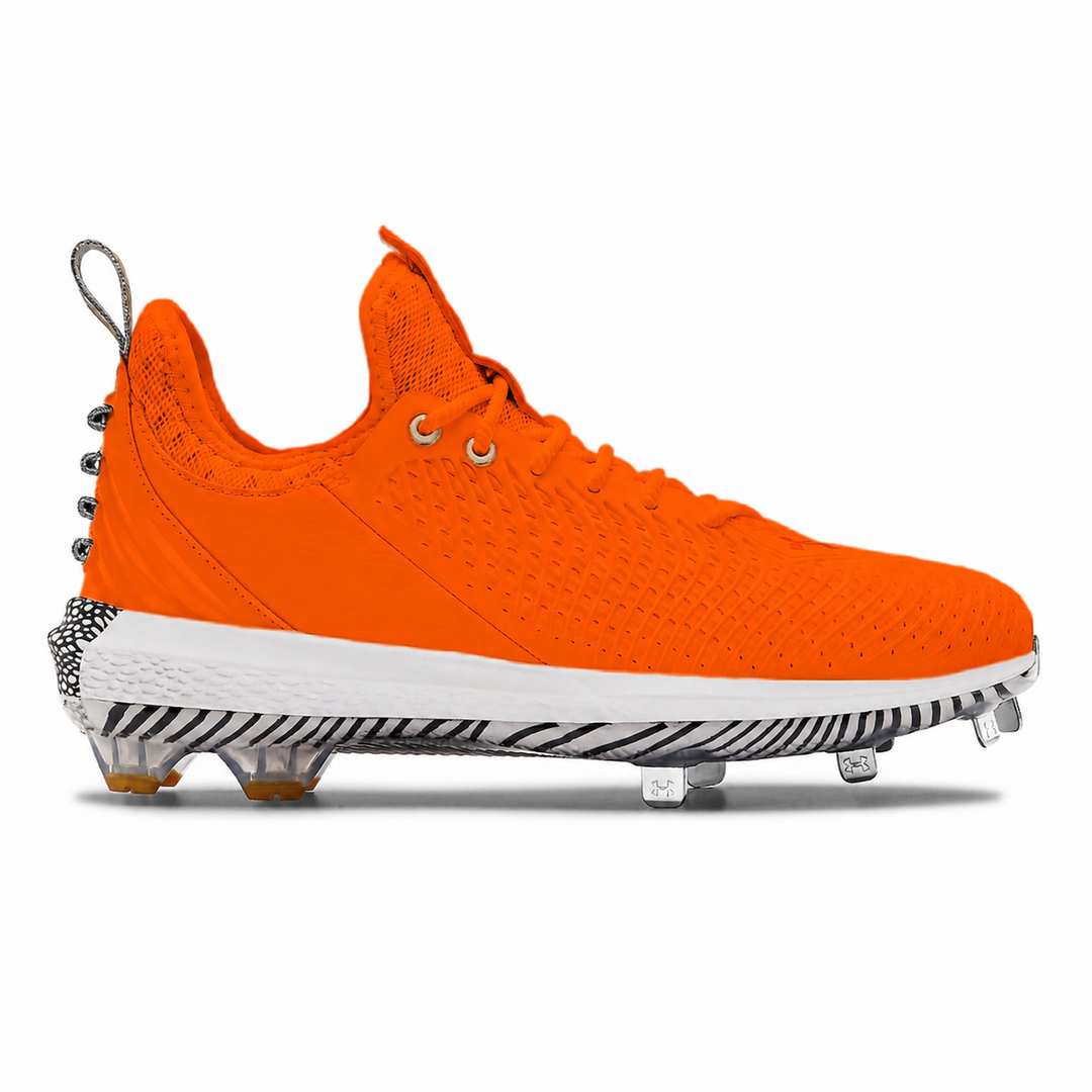 A bright orange baseball cleat with a white midsole and black-and-white zebra-stripe pattern on the outsole, shown in a side profile on a white background.