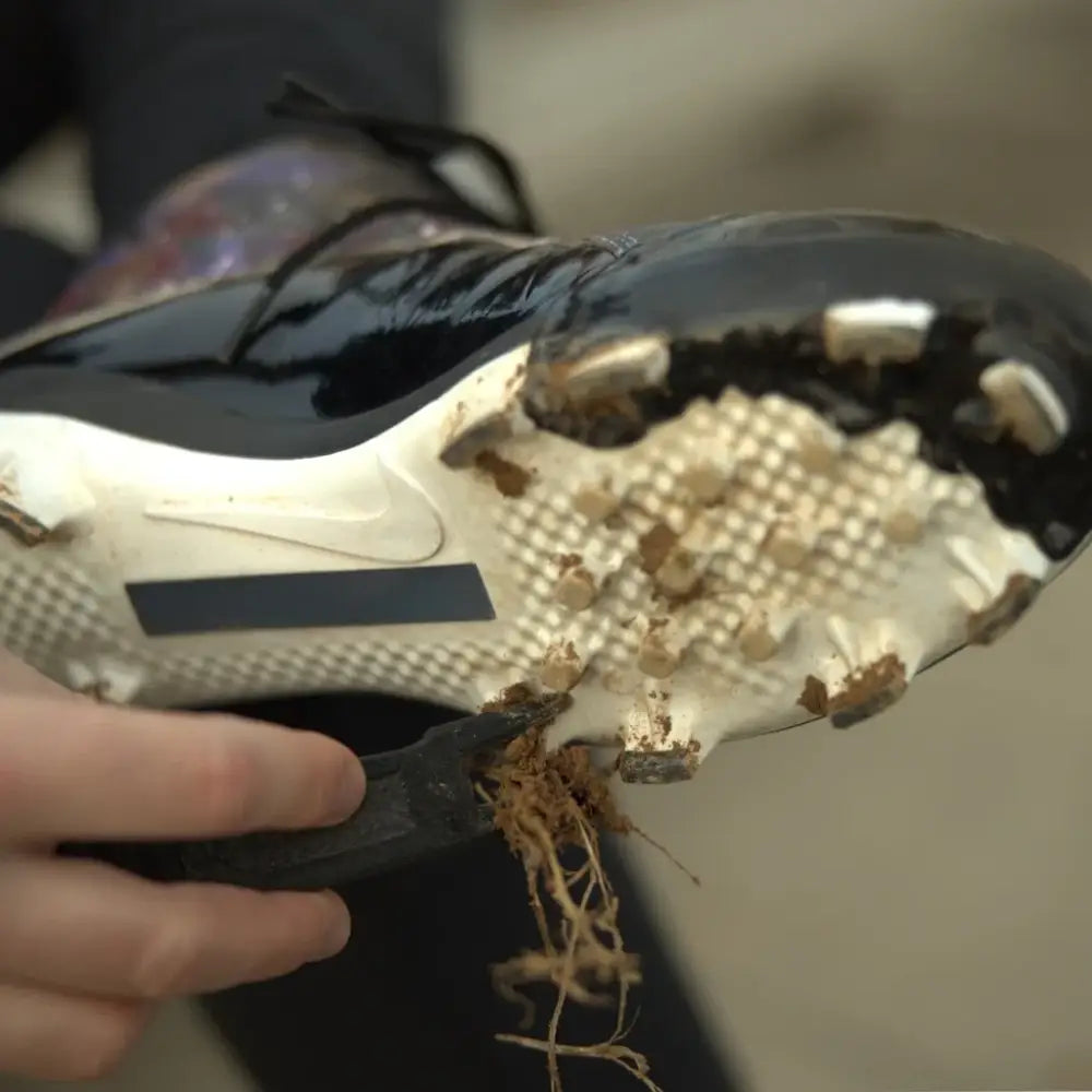 Muddy black and white cleat cleaned with CleatClear™ cleaning tool