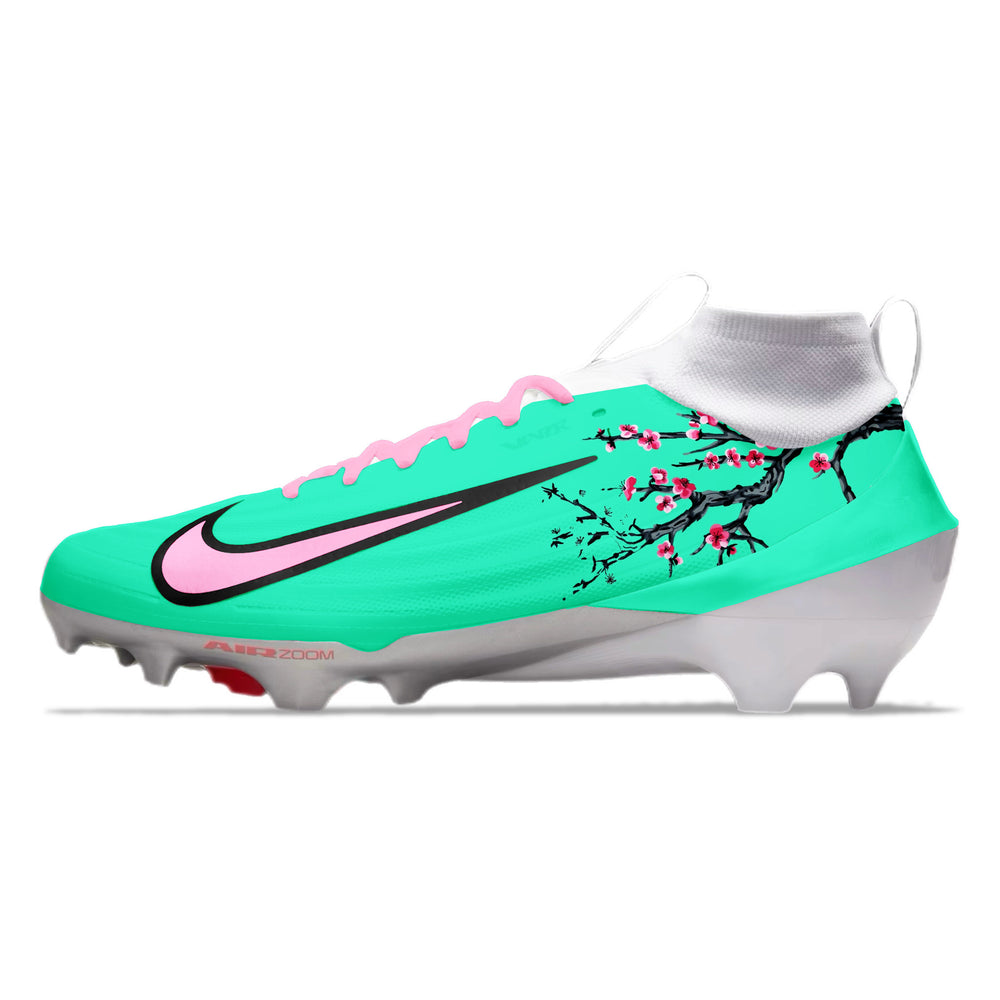 Green football cleats with pink accents and cherry blossom design on a white background