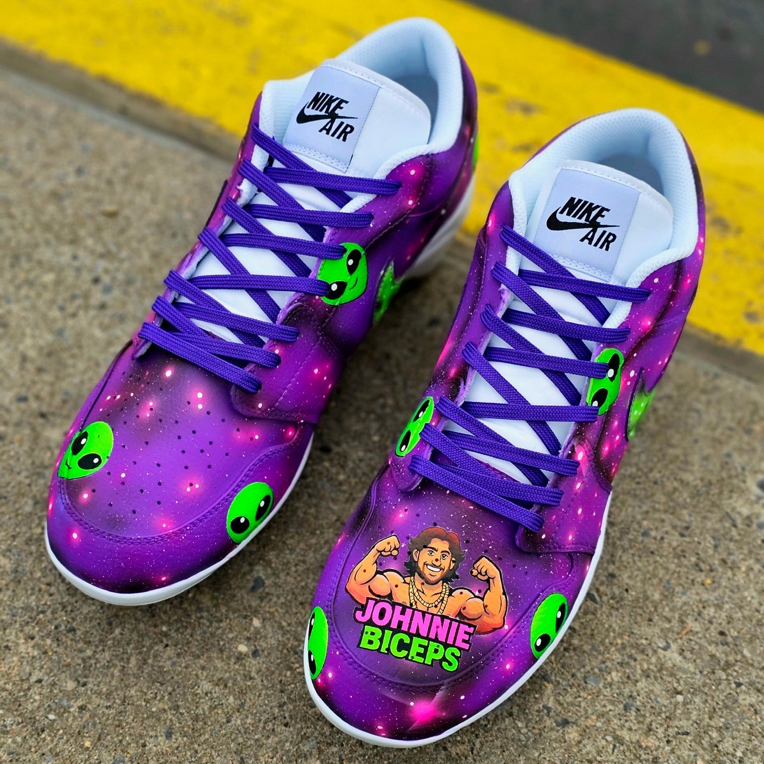 Purple baseball cleats with green accents and 'Johnnie Biceps' graphic on a concrete surface.