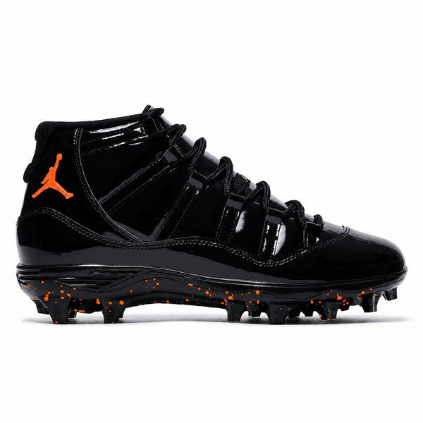  Molten Black Jordan 11 Retro TD football cleats featuring a glossy black patent leather upper, black ballistic mesh side panels, bright orange embroidered Jumpman logo on the ankle, black lace-up closure, and a black midsole with orange speckled molded traction outsole by Staium Custom Kicks.