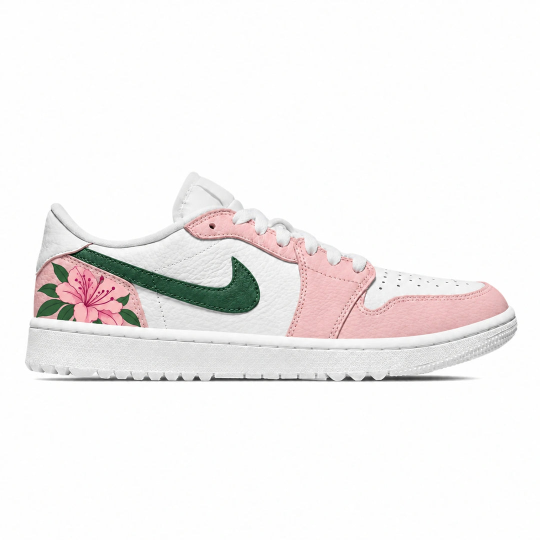 A Jordan low top golf shoe in white and pink suede, featuring a green Swoosh and a pink hazalea flower graphic on the heel.