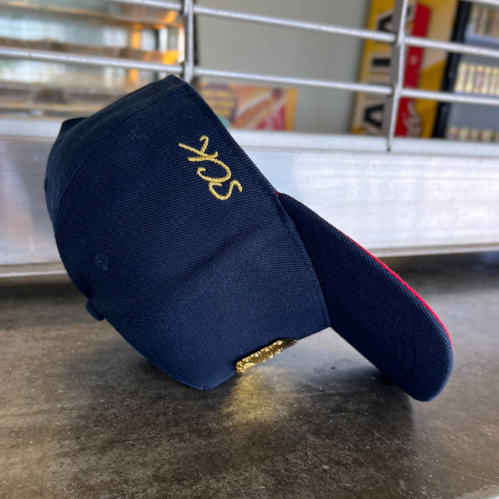 Navy blue cap with gold embroidery on a metallic surface