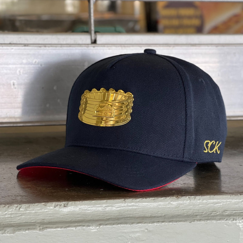 A navy blue snapback hat with a metallic gold SCK logo on the front, with gold embroidery and red accents.