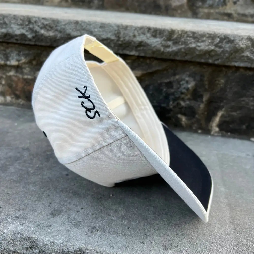 A cream white snapback hat with SCK script wording embroidered on the side.