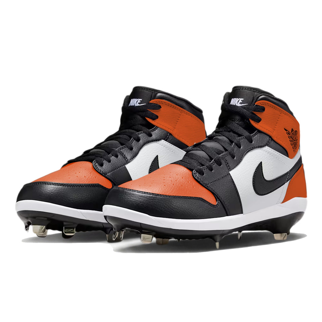 Angled view of Jordan 1 Retro baseball cleats in the Shattered Backboard color way, showcasing orange and black leather panels, white midsole, metal spikes, and hand-painted custom design by Stadium Custom Kicks.