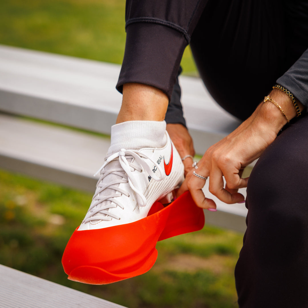 Person wearing a white sneaker with a red sole, sitting on a bench outdoors.