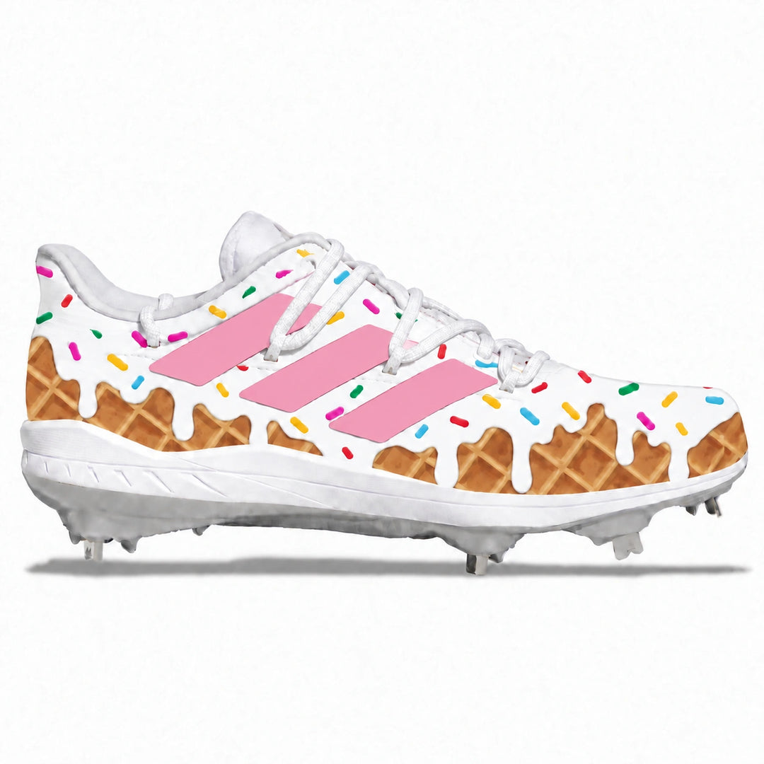 A white baseball cleat featuring a whimsical ice cream and waffle theme, with pink stripes, dripping white frosting, colorful sprinkles, and brown waffle patterns, shown against a plain white background.