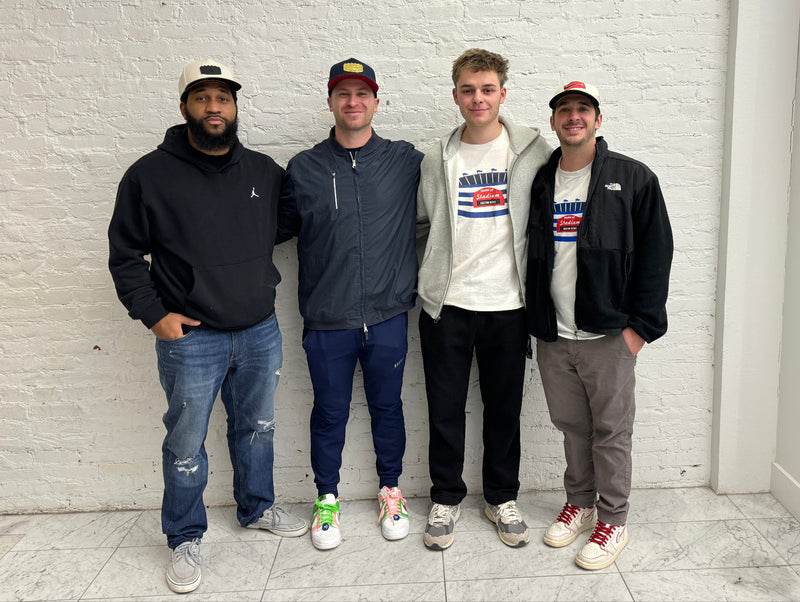 Four men posing together in front of a white brick wall.