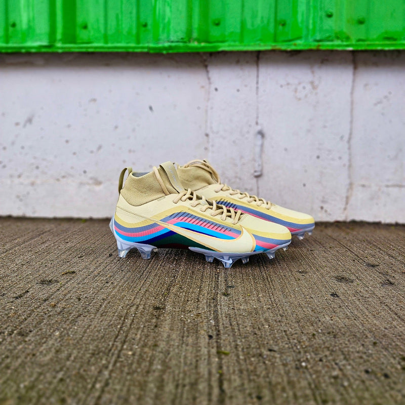 Pair of yellow football cleats with colorful accents on a textured surface with a green metal sheet in the background.